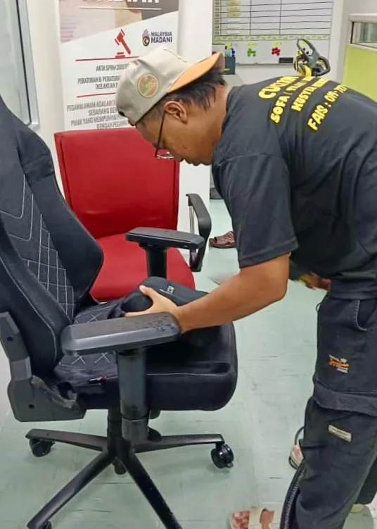 Pekerja mencuci kerusi pejabat berwarna merah dan hitam dengan alat ekstraksi