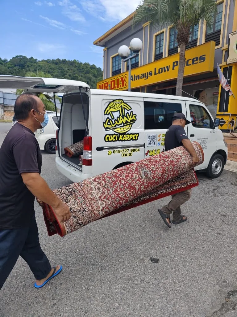 Dua pekerja mengangkat karpet rumah yang digulung ke dalam van Kluang Cuci Karpet